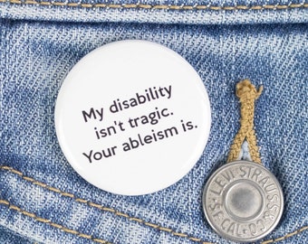 Può includere: Un bottone bianco con il testo "My disability isn't tragic. Your ableism is." appuntato su una giacca di jeans blu.