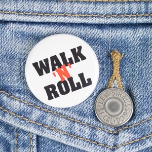 May include: A white button with black text that reads "Walk 'N Roll" pinned to a blue denim jacket.