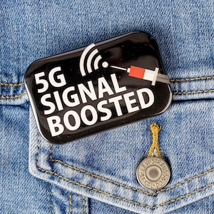May include: A black button with a white 5G signal boosted text and a red and white syringe graphic on a blue denim jacket.