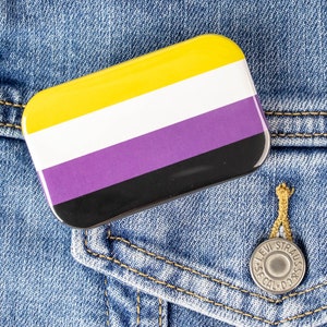 Peut inclure: Une épingle rayée jaune, blanche, violette, noire et noire sur une veste en jean bleue.