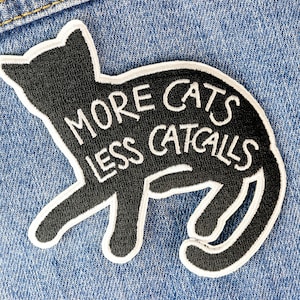 May include: Black iron-on patch with a black cat silhouette and white text that reads "More Cats Less Catcalls".
