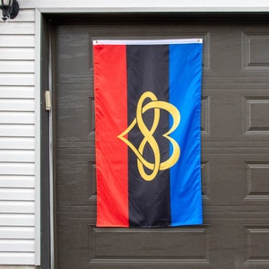 May include: A black, red and blue flag with a gold infinity symbol in the shape of two hearts. The flag is hanging on a garage door.