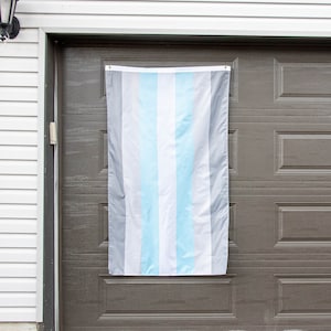 May include: A light blue, white, and gray striped flag hanging on a brown garage door.