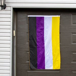 May include: A purple, white and yellow flag with black stripes hanging on a brown garage door. The flag is made of fabric and has a slightly textured surface.