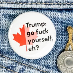 May include: A white button with a red and white Canadian flag and the text "Trump: go fuck yourself, eh?"
