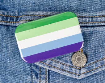 Puede incluir: Un pin rayado verde, blanco, azul claro y morado en una chaqueta vaquera azul.