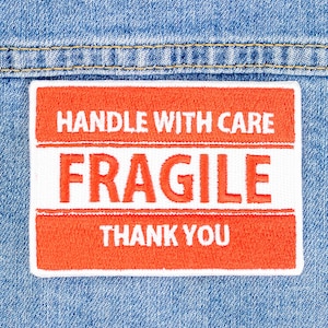 May include: A red and white fragile sticker with the text "HANDLE WITH CARE" and "FRAGILE" in white lettering and "THANK YOU" in red lettering.