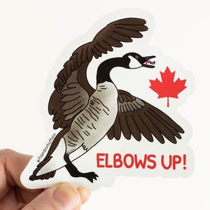 May include: A sticker featuring a cartoon illustration of a Canada goose with its wings spread, a red maple leaf, and the text "Elbows Up!"