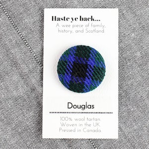 Peut inclure: Un petit bouton rond avec un motif tartan bleu, vert et noir. Le bouton est sur une carte blanche avec le texte "Haste ye back... A wee piece of family, history, and Scotland. Douglas 100% wool tartan. Woven in the UK. Pressed in Canada."