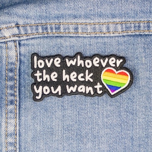 May include: A black and white embroidered patch on a blue denim background. The patch says "love whoever the heck you want" with a rainbow heart.