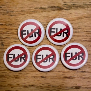 Könnte beinhalten: Fünf weiße runde Knöpfe mit einem roten Kreis und einer diagonalen schwarzen Linie, die ihn durchschneidet. Das Wort "FUR" ist in schwarzen Buchstaben innerhalb des Kreises geschrieben. Die Knöpfe befinden sich auf einer Holzoberfläche.