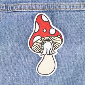Op de afbeelding: Een geborduurde rode en witte paddenstoel patch met een witte steel. De patch is genaaid op een blauw denim jack.