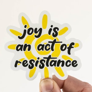 May include: A yellow sun sticker with the text "joy is an act of resistance" in black.