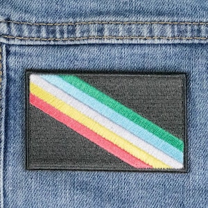 Puede incluir: Un parche negro con un diseño de franja de arcoíris diagonal. La franja está hecha de cinco colores: verde, azul claro, blanco, amarillo y rojo.