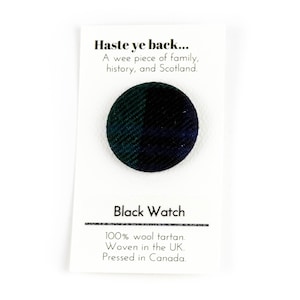 Op de afbeelding: Een kleine ronde knoop met een Black Watch tartan patroon. De knoop is op een witte kaart met de tekst "Haste ye back... A wee piece of family, history, and Scotland. Black Watch 100% wool tartan. Woven in the UK. Pressed in Canada."