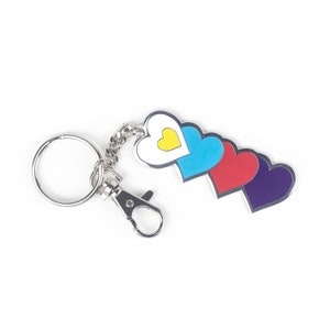 Op de afbeelding: Een zilveren sleutelhanger met een zilveren ring en een zilveren clip. De sleutelhanger heeft vier in elkaar grijpende harten, een wit met een geel midden, een blauw, een rood en een paars.