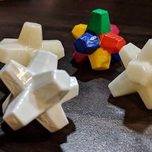May include: Four white star-shaped geometric objects with a multi-colored geometric object in the center. The multi-colored object is made of six pieces, each a different color: red, green, blue, yellow, purple, and orange.