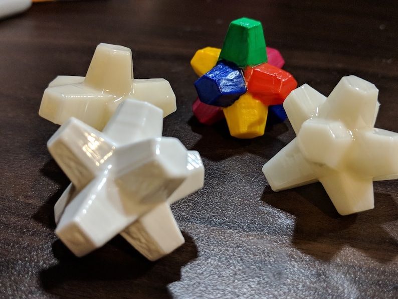 May include: Four white star-shaped geometric objects with a multi-colored geometric object in the center. The multi-colored object is made of six pieces, each a different color: red, green, blue, yellow, purple, and orange.