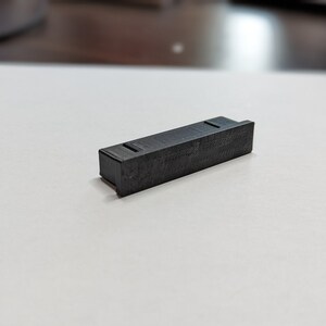May include: A black plastic rectangular block with a textured surface.