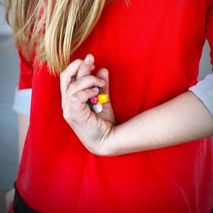 May include: A close-up of a person's hand holding a small group of colorful candy. The candy is red, yellow, blue, and green.
