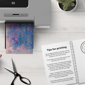 K&ouml;nnte beinhalten: Nahaufnahme eines Druckers mit einem Blatt Papier mit einem abstrakten floralen Design in Blau und Rosa. Das Papier wird in den Drucker eingezogen. Der Text auf der Seite lautet "Tipps zum Drucken" und enth&auml;lt Anweisungen zum Drucken der digitalen Papiere.