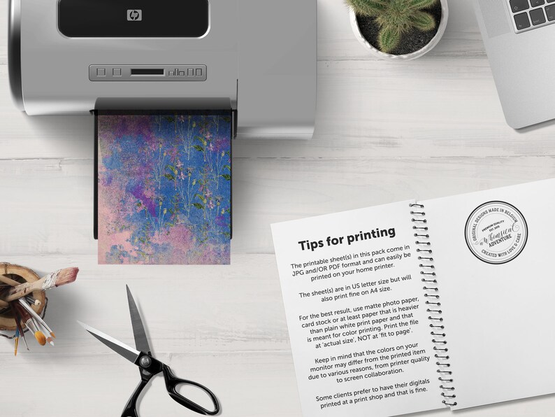 K&ouml;nnte beinhalten: Nahaufnahme eines Druckers mit einem Blatt Papier mit einem abstrakten floralen Design in Blau und Rosa. Das Papier wird in den Drucker eingezogen. Der Text auf der Seite lautet "Tipps zum Drucken" und enth&auml;lt Anweisungen zum Drucken der digitalen Papiere.