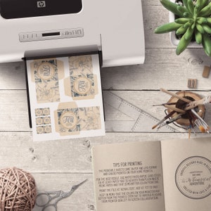 May include: Printable tea box labels with a vintage design. The labels feature a floral pattern with the word "Tea" in a circle. The labels are printed on a light brown paper with a textured surface. The labels are designed to be printed at home.