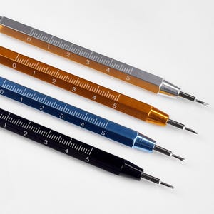 May include: Four watch repair tools in silver, gold, blue, and black. Each tool has a ruler with markings from 0 to 5. The tools are designed for precision work and are set against a white background.