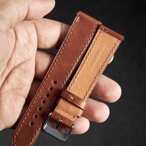 May include: A brown leather watch strap with stitching detail and a silver buckle. The strap is labeled "Full Grain Leather Handmade".