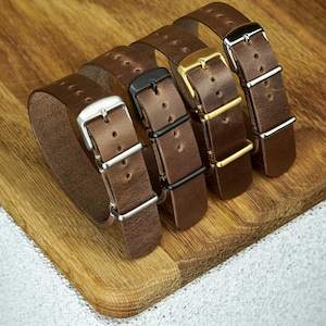 Peut inclure: Quatre bracelets de montre en cuir marron disposés en rangée. Chaque bracelet présente une finition de boucle en métal différente : argent, noir mat, doré et chrome poli. Les bracelets ont des coutures visibles et plusieurs trous.