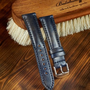 May include: Two dark blue leather watch straps with white stitching and silver buckles. The straps are on a wooden surface with a brush and the text "Balabanoff refined leather goods".