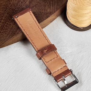 May include: A brown leather watch strap with stitching detail and a silver buckle. The strap is labeled "Full-grain leather Handmade in Italy".