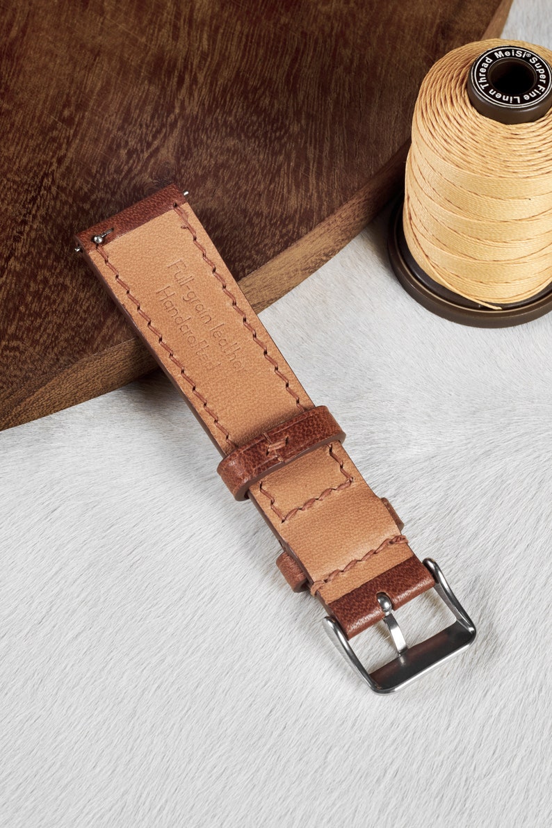 May include: A brown leather watch strap with stitching detail and a silver buckle. The strap is labeled "Full-grain leather Handmade in Italy".