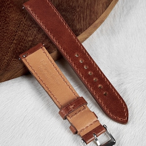 May include: Two brown leather watch straps with stitching detail. One strap has a silver buckle and the text "Full grain leather Handmade in Italy" printed on the inside.