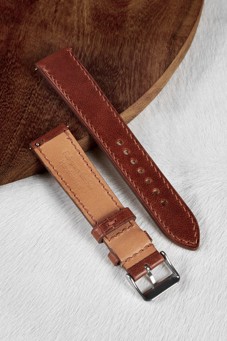 May include: Two brown leather watch straps with stitching detail. One strap has a silver buckle and the text "Full grain leather Handmade in Italy" printed on the inside.