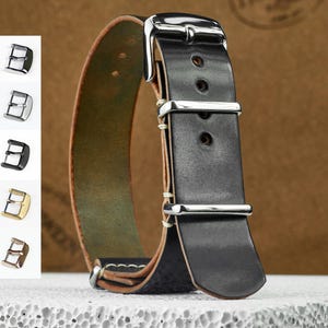 Puede incluir: Correa de reloj de cuero negro con hebilla y presillas plateadas. La correa tiene costuras blancas y una parte inferior marrón. La imagen también muestra una selección de hebillas.