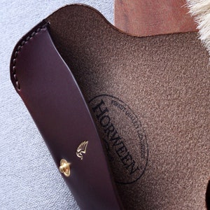 May include: A brown leather case with a gold winged logo and the text "Horween" in a circle. The case is lined with a brown suede material.