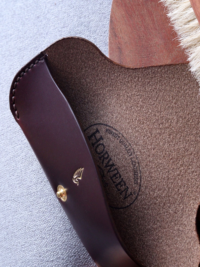 May include: A brown leather case with a gold winged logo and the text "Horween" in a circle. The case is lined with a brown suede material.