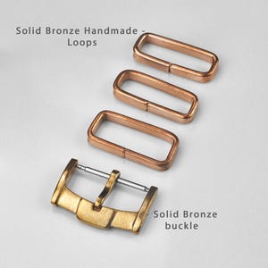 Puede incluir: Un conjunto de componentes de reloj de bronce macizo, que incluye tres bucles rectangulares y una hebilla. Los bucles son de un cálido color cobre, mientras que la hebilla tiene un acabado dorado. El texto en la imagen dice "Solid Bronze Handmade Loops" y "Solid Bronze buckle."