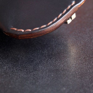 May include: Close-up of a black leather wallet with a brown stitched edge. The wallet is lying on a dark textured surface.