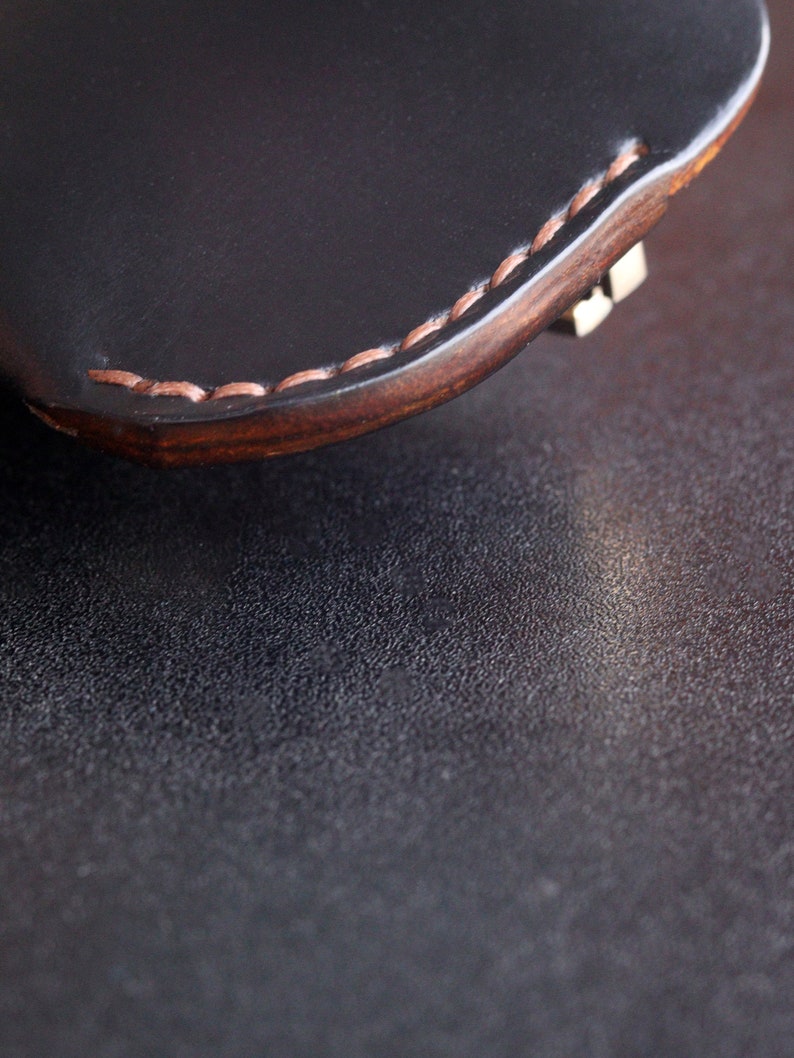 May include: Close-up of a black leather wallet with a brown stitched edge. The wallet is lying on a dark textured surface.