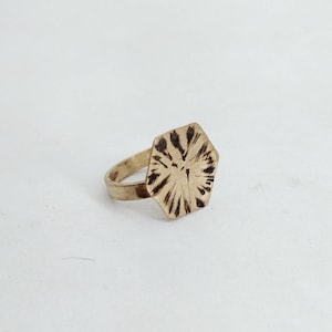 Peut inclure: Une bague hexagonale en or avec un motif texturé. La bague est en métal et a une bande simple.