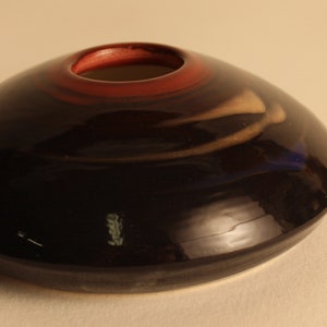 May include: A dark blue ceramic vase with a wide, shallow shape and a red interior rim. The vase has a glossy finish and a small opening at the top. A coin is next to the vase for size comparison.