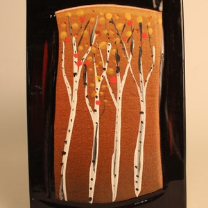 May include: A black framed ceramic tile with a painted image of white birch trees with red and yellow accents on a brown background.