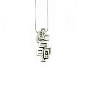 Könnte beinhalten: Eine silberne Halskette mit einem geometrischen Anhänger aus ineinandergreifenden Quadraten.