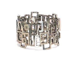 Puede incluir: Un brazalete de plata hecho de formas cuadradas entrelazadas.