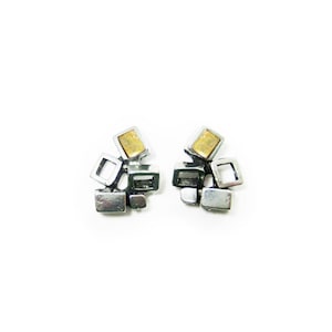May include: A pair of silver earrings with a cluster of small, geometric shapes. Each earring features a single, larger square with a yellow centre.