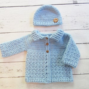 May include: A light blue crocheted baby cardigan with a matching hat. The cardigan has a button closure and a collar. The hat has a wooden button.