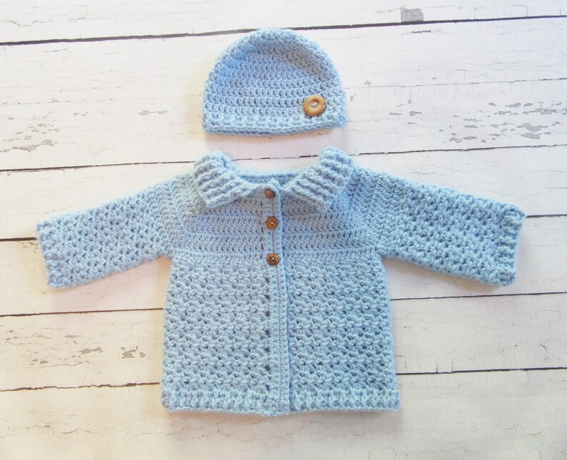 May include: A light blue crocheted baby cardigan with a matching hat. The cardigan has a collar and buttons down the front. The hat has a button on top.