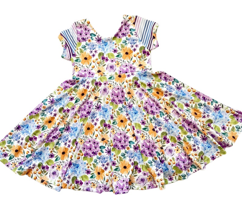 May include: A white dress with a floral print featuring purple, blue, yellow, and green flowers. The dress has short sleeves with a striped pattern on the sleeves.